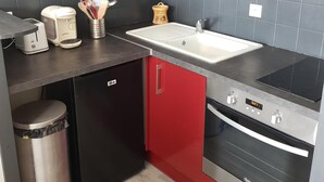Eine kleine Küche mit roten Schränken, einem schwarzen Geschirrspüler, einer Edelstahl-Spüle und einem eingebauten Backofen.