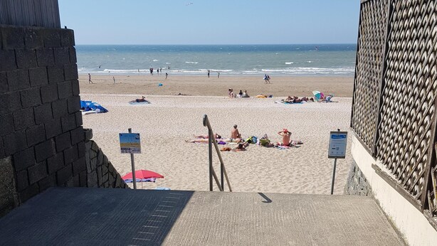 Ein Strand mit einer gepflasterten Promenade, die zum Ufer führt, mit einem Wegweiser und einem Holzzaun.