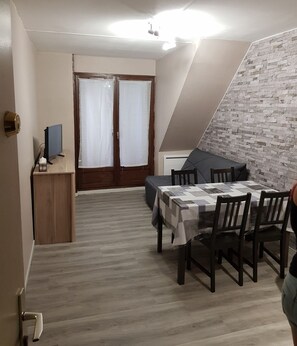 Un coin repas avec une table dressée pour quatre personnes, un bureau en bois avec un ordinateur, et une vue sur un mur de briques.