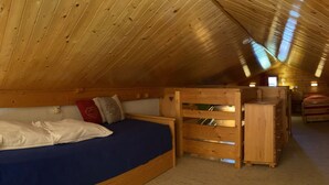 A cozy attic bedroom with a curved bed, wooden headboard, and a built-in wooden chest of drawers.