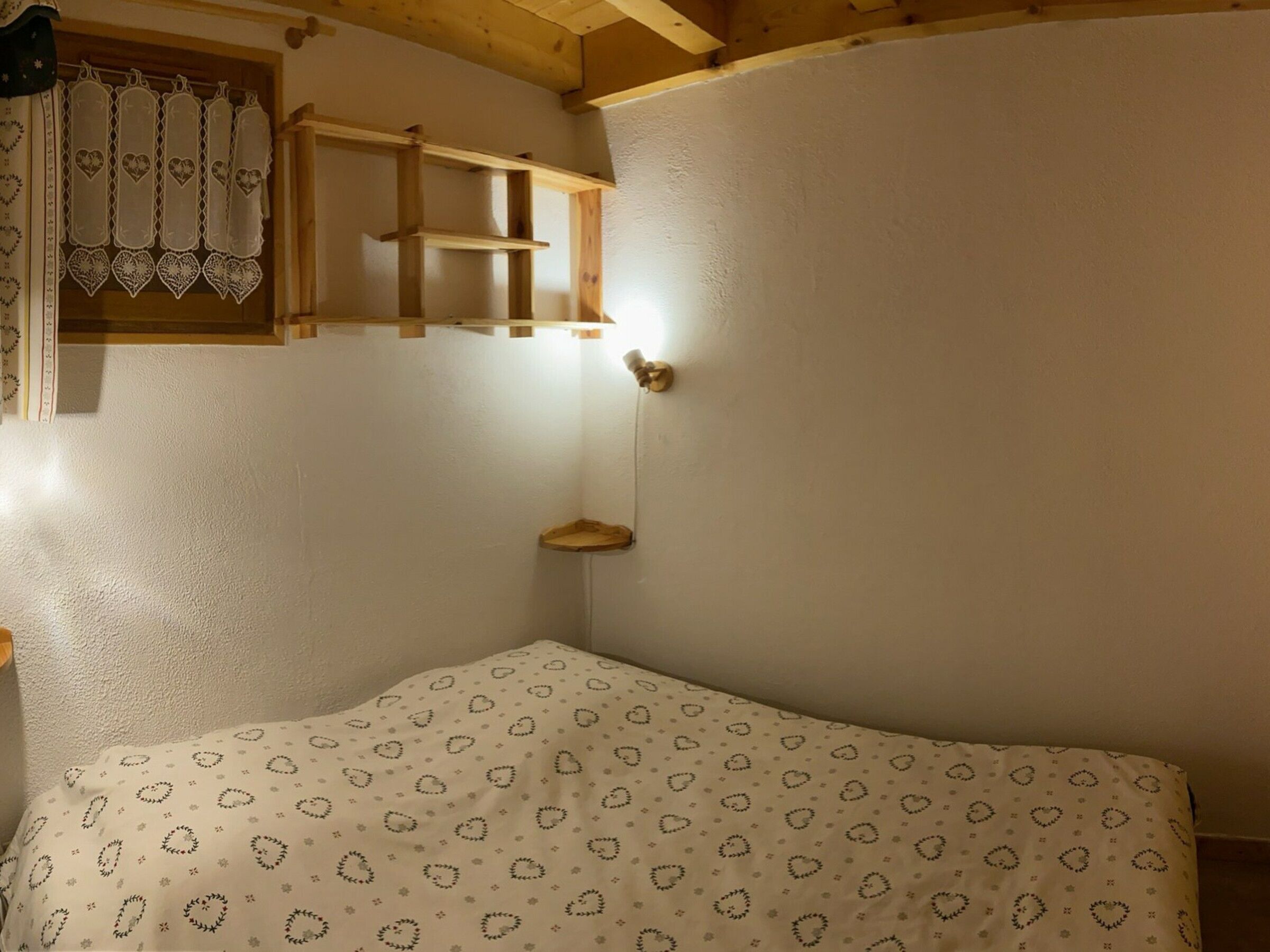 A bedroom with a bed, a wooden shelf, and a wall-mounted light.