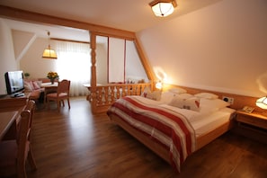 Une chambre à coucher avec un lit en bois, un bureau avec une chaise, une télévision et un balcon doté d’une balustrade.