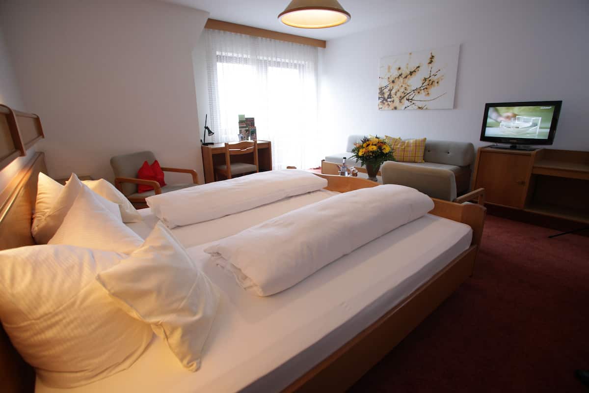 Habitación de hotel con cama, escritorio, silla, televisor y ventana con cortinas.