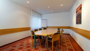 A conference room with a round table, eight chairs, a whiteboard, and a patterned carpet.
