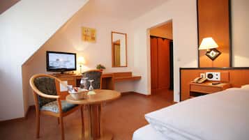 Une chambre d’hôtel comprenant un lit, un bureau avec une télévision, une chaise, une table avec une lampe et un miroir.
