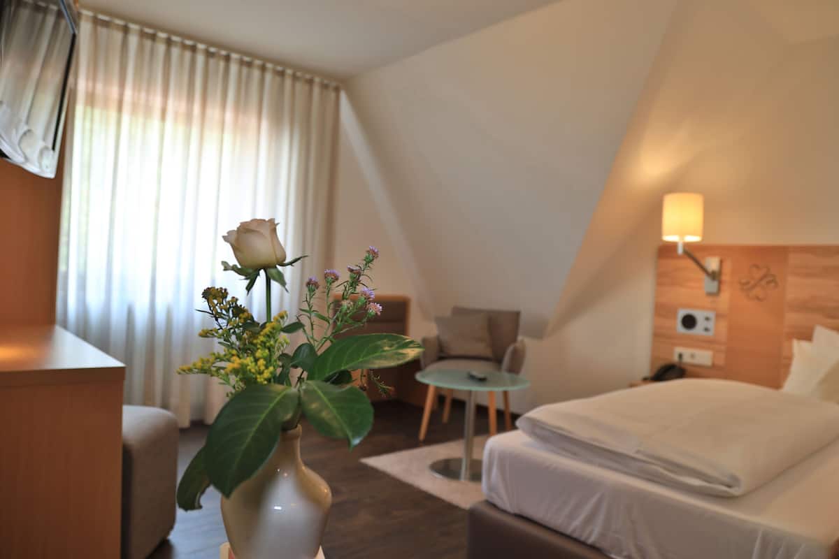 Habitación de hotel con cama, una mesita, una silla, un escritorio y un florero con flores.
