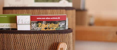 A wicker basket with a wooden spoon inside, containing a book titled "Zum Alten Schloss" and a sign with the website "www.zum-alten-schloss.de".