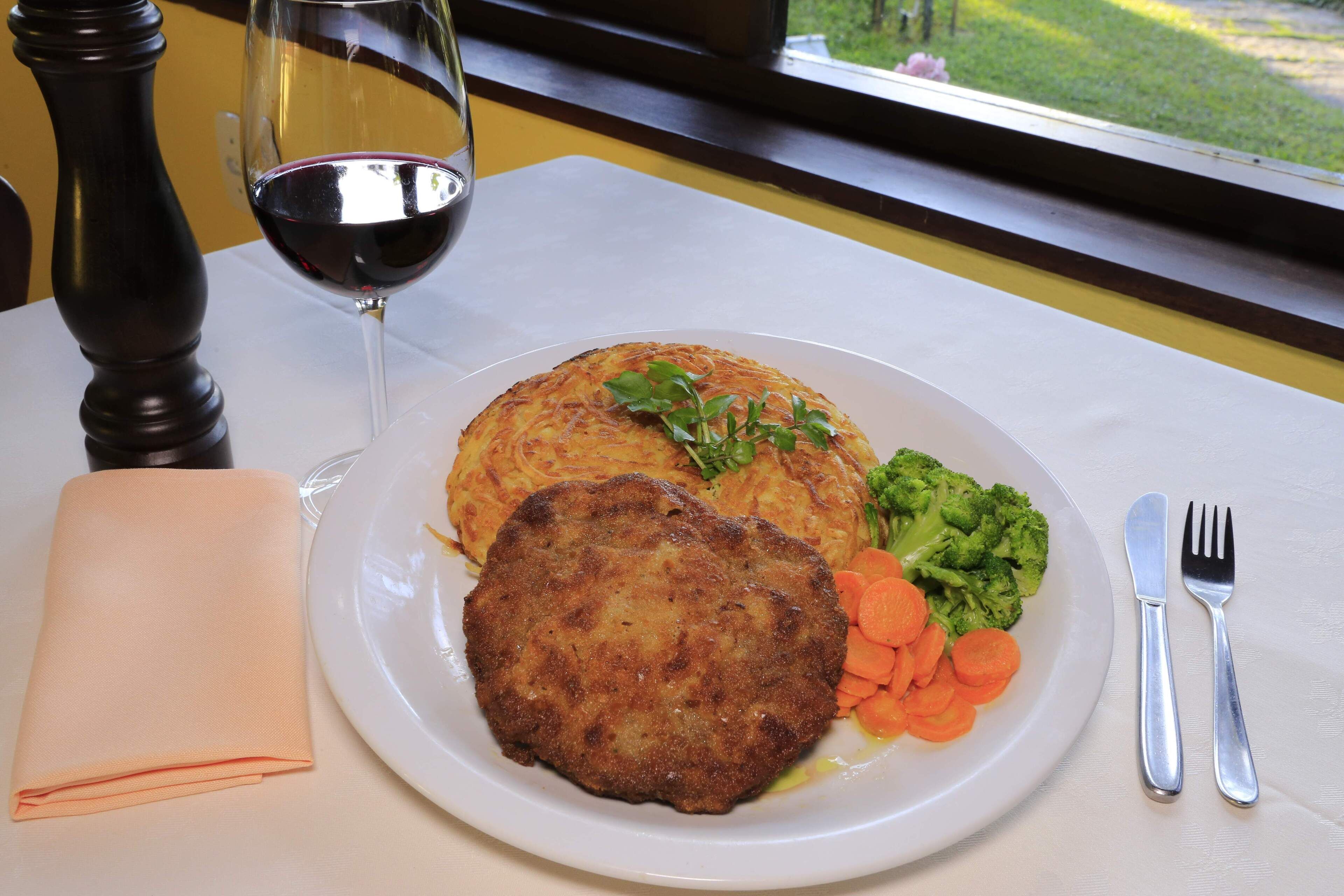 Un plato con comida, una copa de vino tinto y una servilleta doblada sobre una mesa.