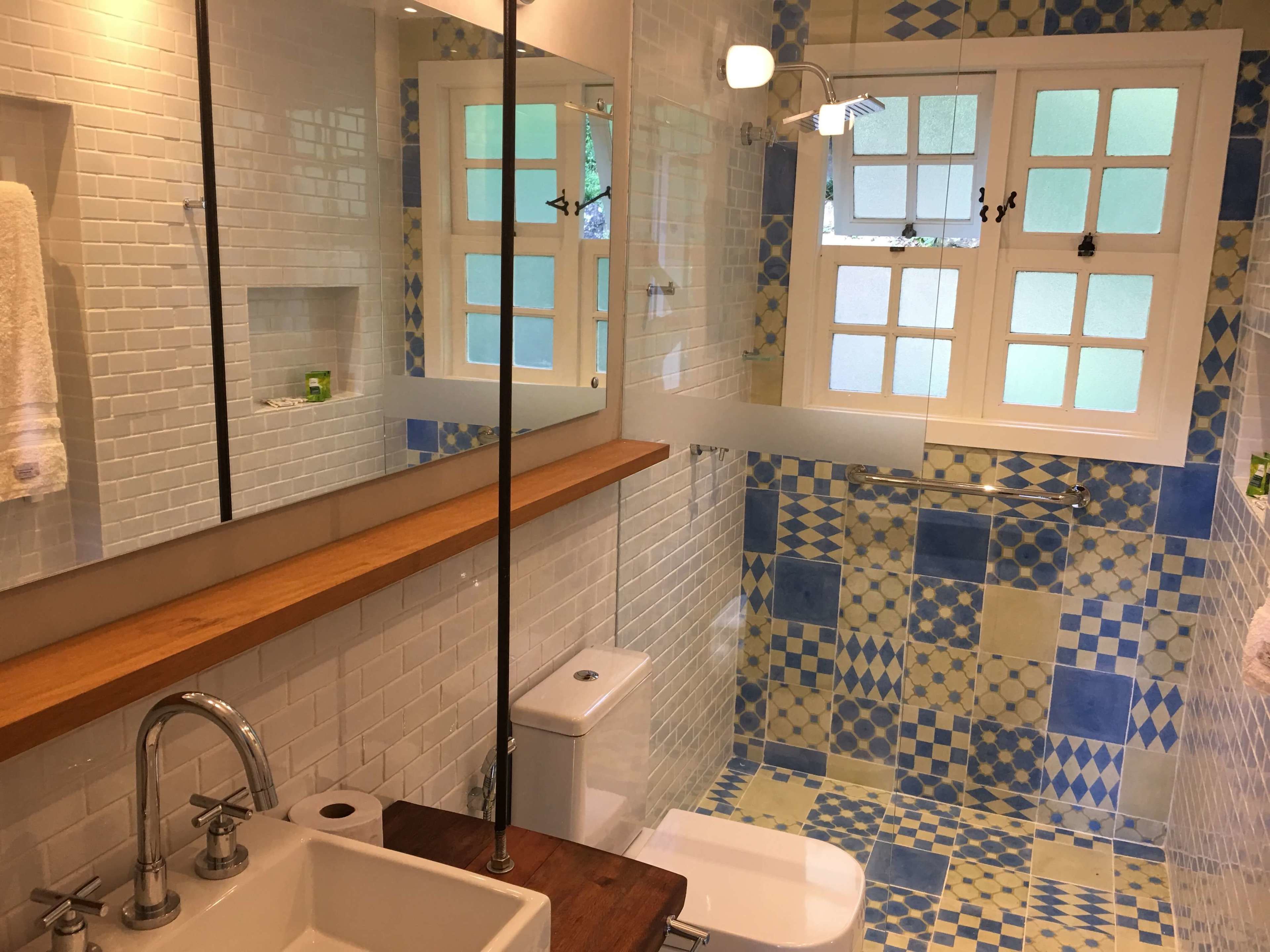 Een badkamer met een wit wastafel, een spiegel, een douche met glazen deur en een raam met uitzicht op bomen.