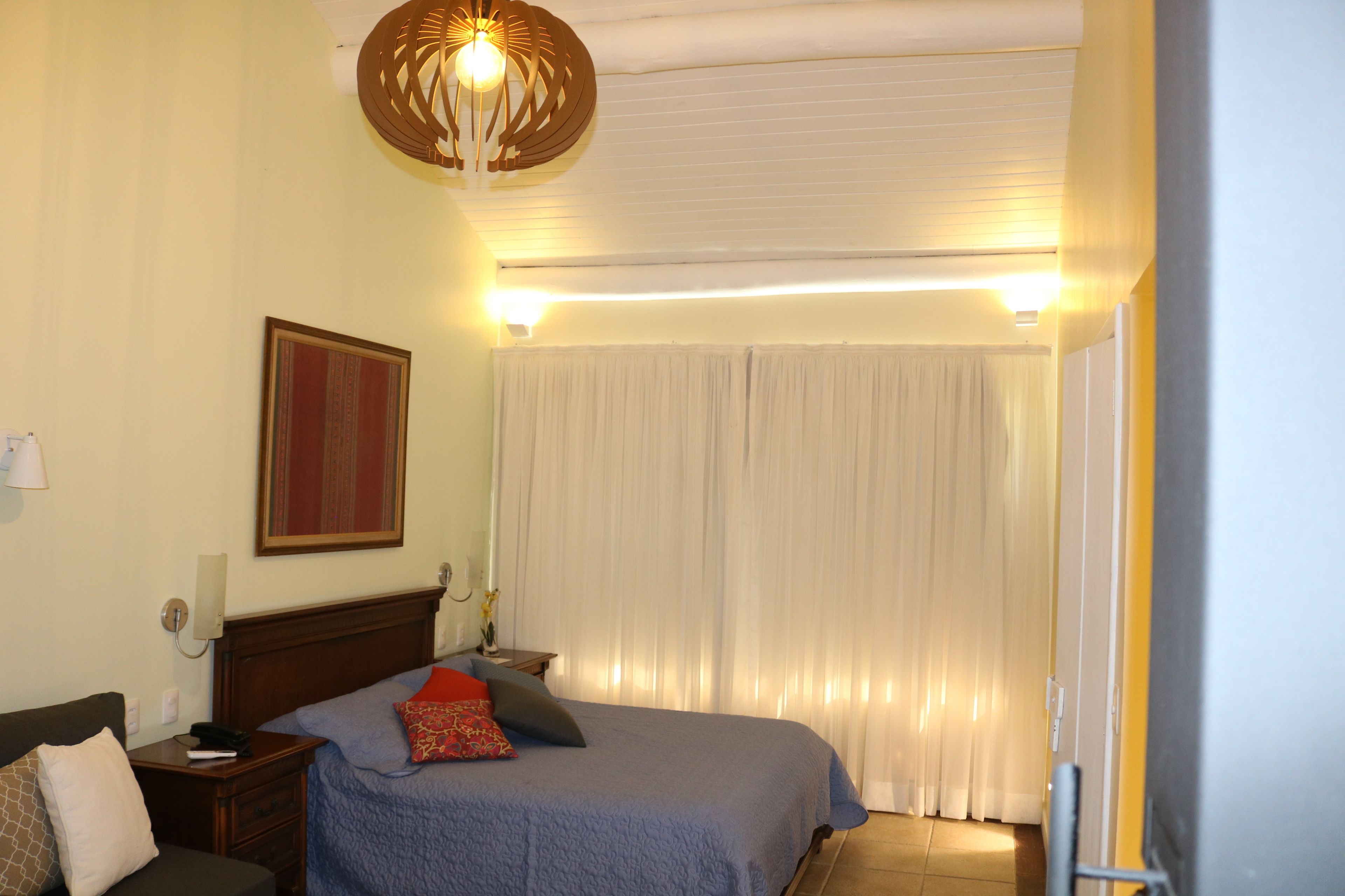 A hotel room with a bed, bedside table, lamp, and curtains.