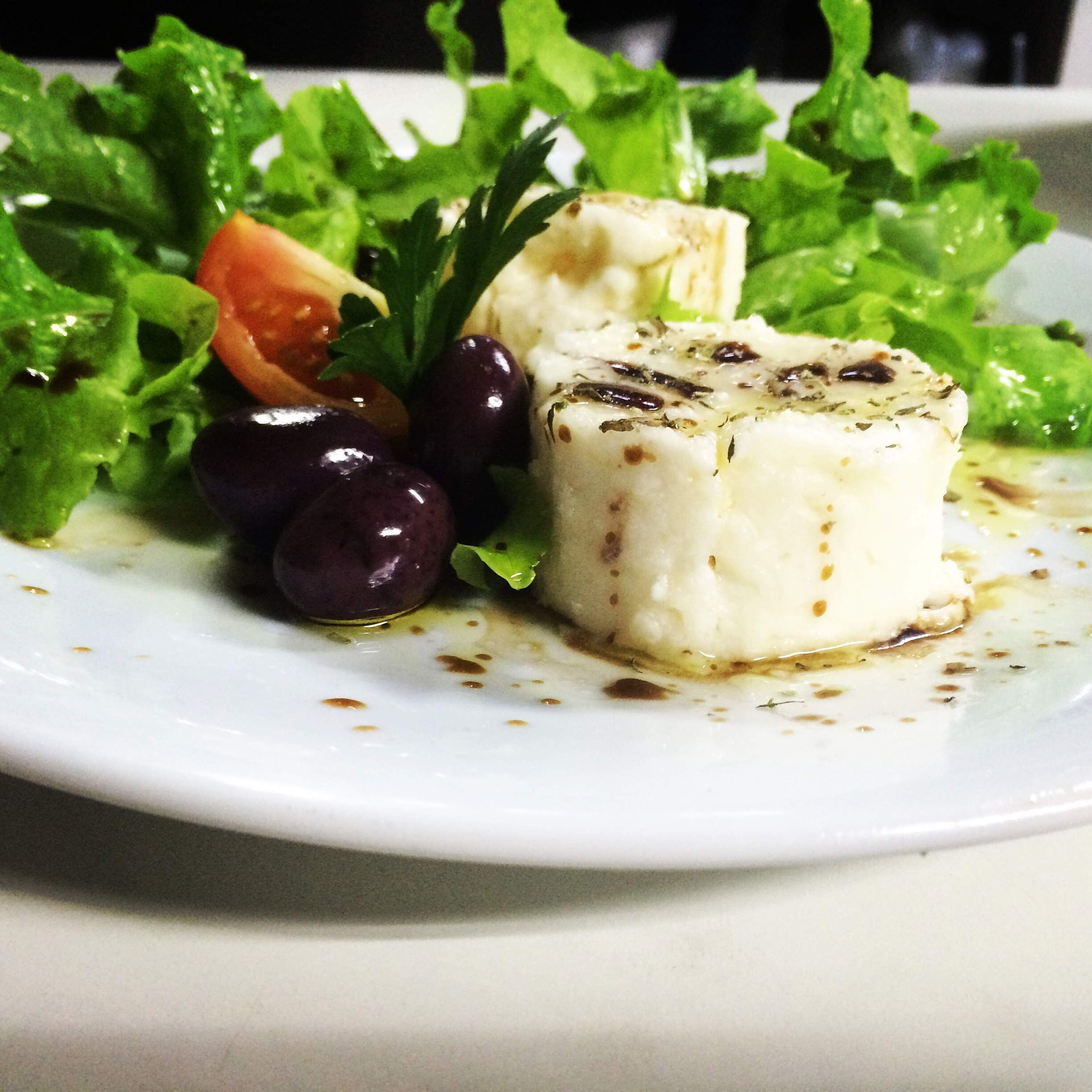 A plate with a white cheese, green salad, and olives.