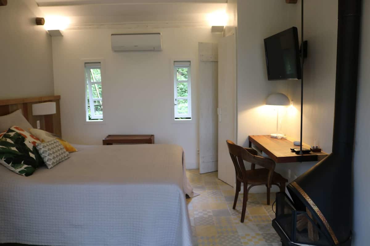 A bedroom with a bed, a desk, a chair, a TV, and two windows.