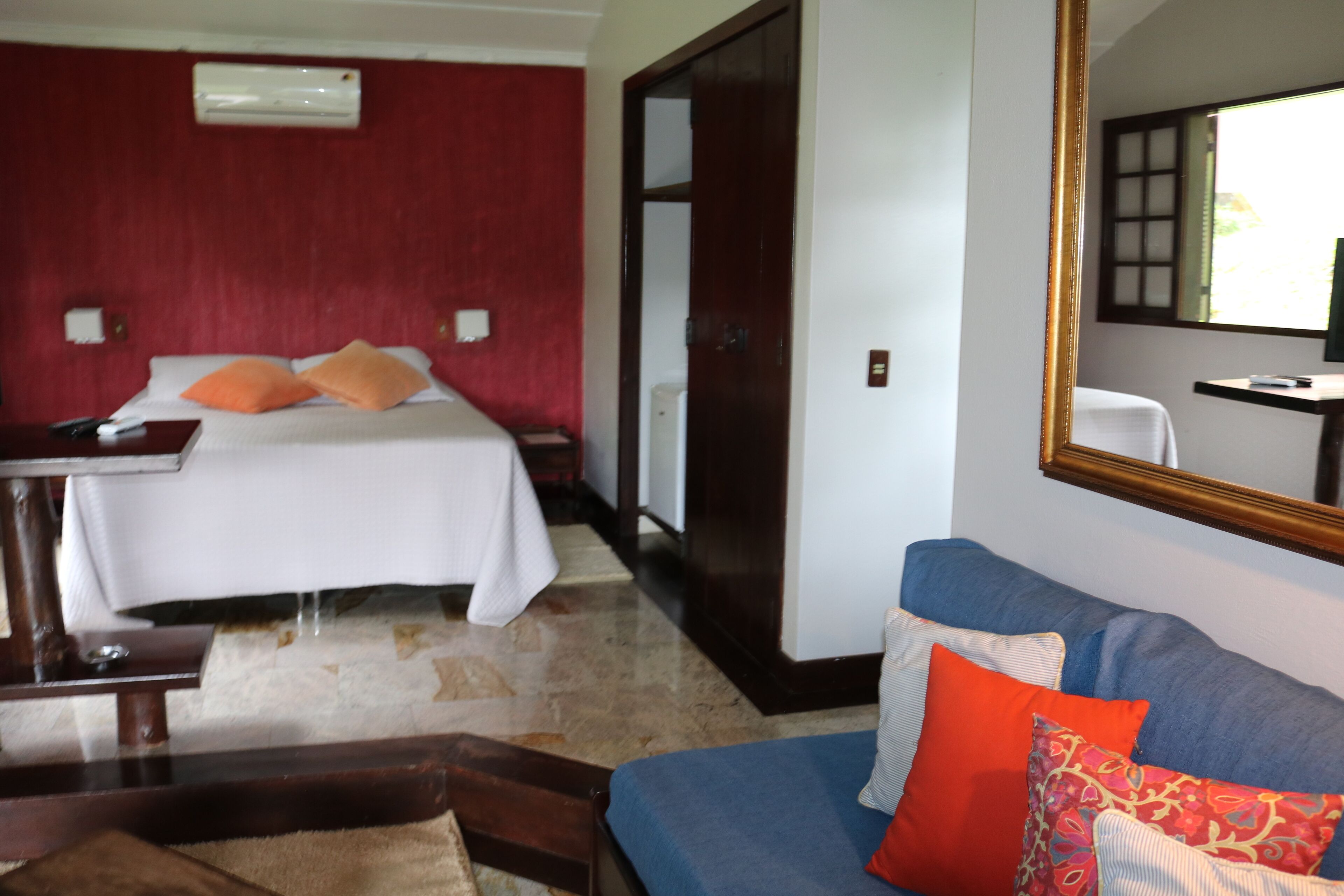 Une chambre d’hôtel avec un lit, un canapé bleu, un miroir et un mur rouge.