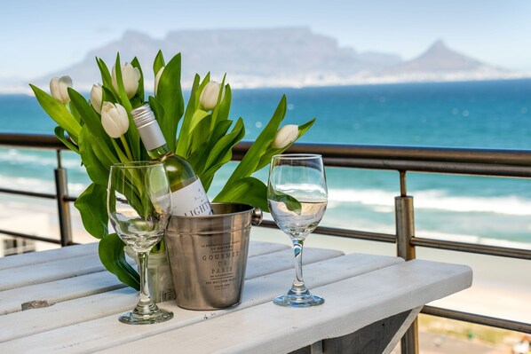 A table with a champagne bottle, a glass, and tulips on a balcony overlooking the ocean.