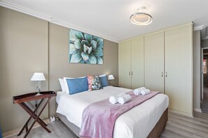A hotel room with a bed, a nightstand, a painting, a wardrobe, and a door leading to another room.