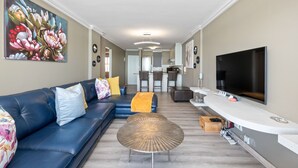 Una sala de estar moderna con un sofá azul, una mesa de centro redonda y un televisor de pantalla plana.