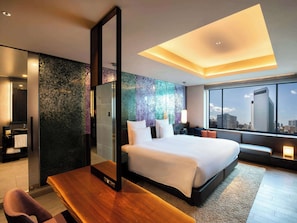 Relax in a spacious room with a large bed, desk, and chair, featuring a unique ceiling design and city views.