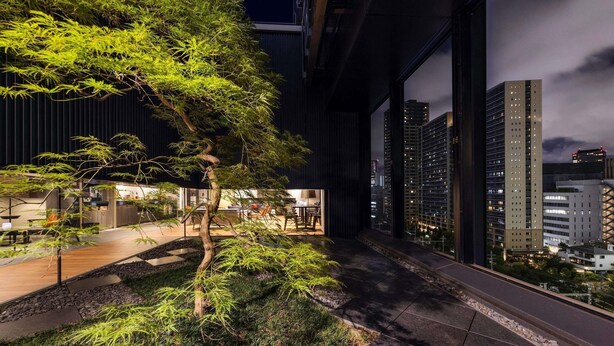 A modern building with a glass facade, a landscaped garden with trees, and a view of the city skyline.
