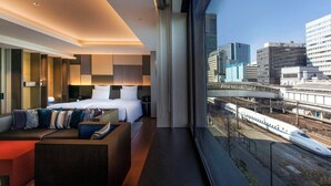Une chambre d’hôtel moderne dotée d’un lit, d’un coin salon et offrant une vue sur la ville grâce à de grandes fenêtres.