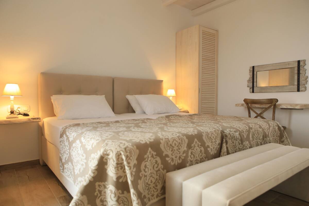 A bedroom with a bed, bedside lamps, a bench, a wardrobe, and a mirror on the wall.