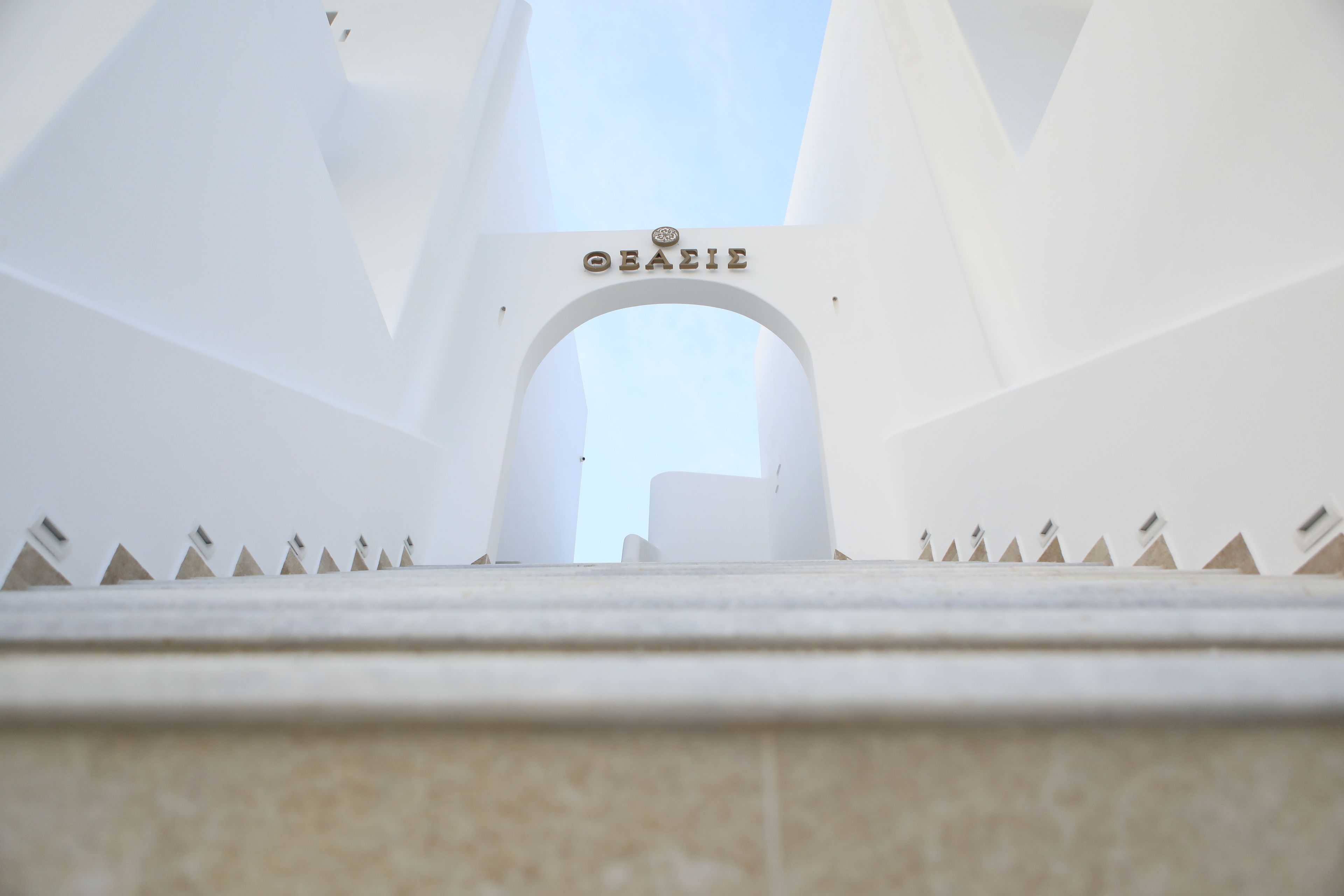 A white arched entrance with the word "OAEANIE" above it, leading into a building with a modern architectural design.