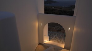 A staircase leading to an outdoor area with a stone floor and a view of the sea and a distant island. - Theasis Luxury Suites (Naxos)