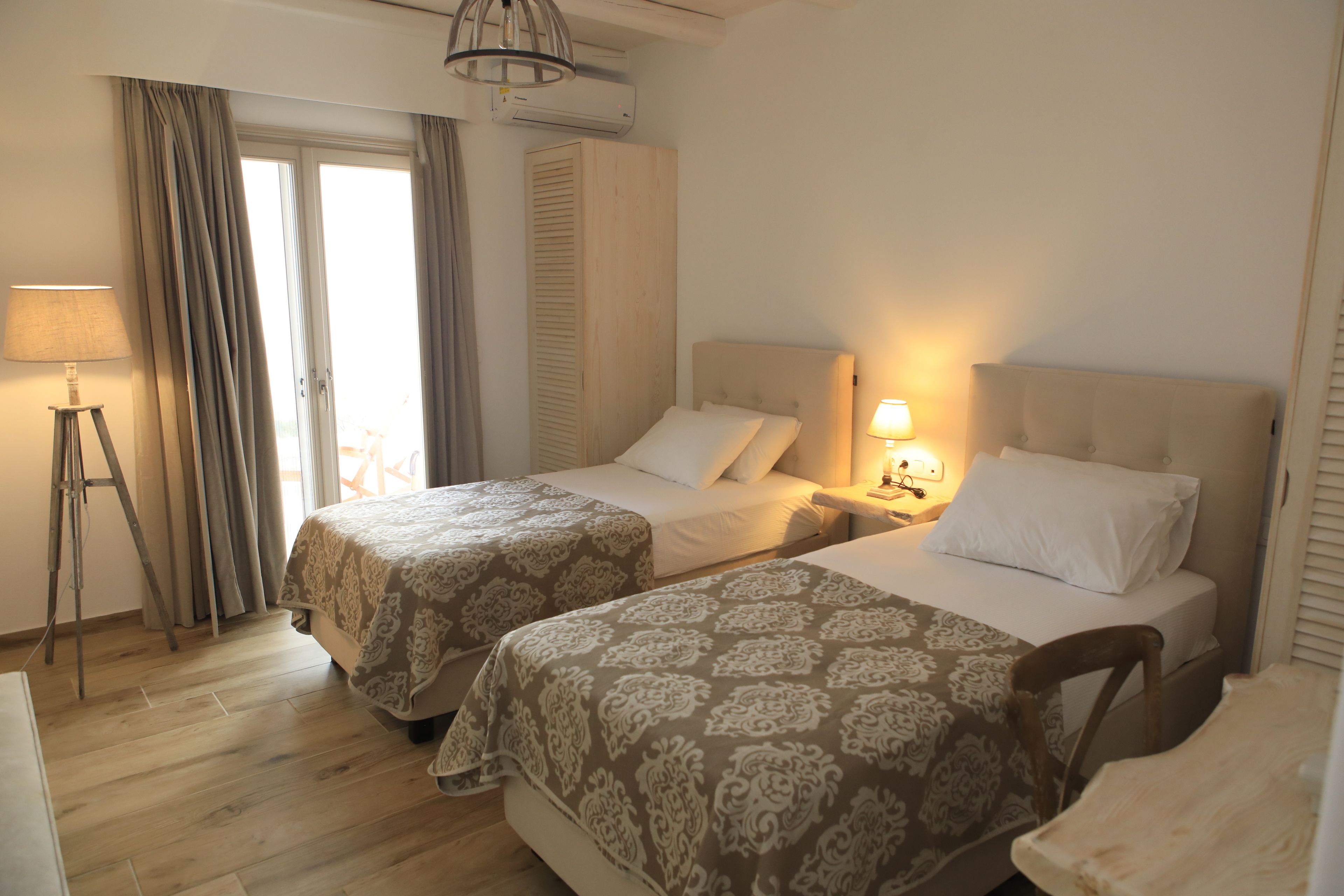 A hotel room with two beds, a desk, a lamp, and a window with curtains.