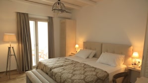 A hotel room with a large bed, bedside lamps, a bench, a desk, and a view of the outdoors. - Theasis Luxury Suites (Naxos)