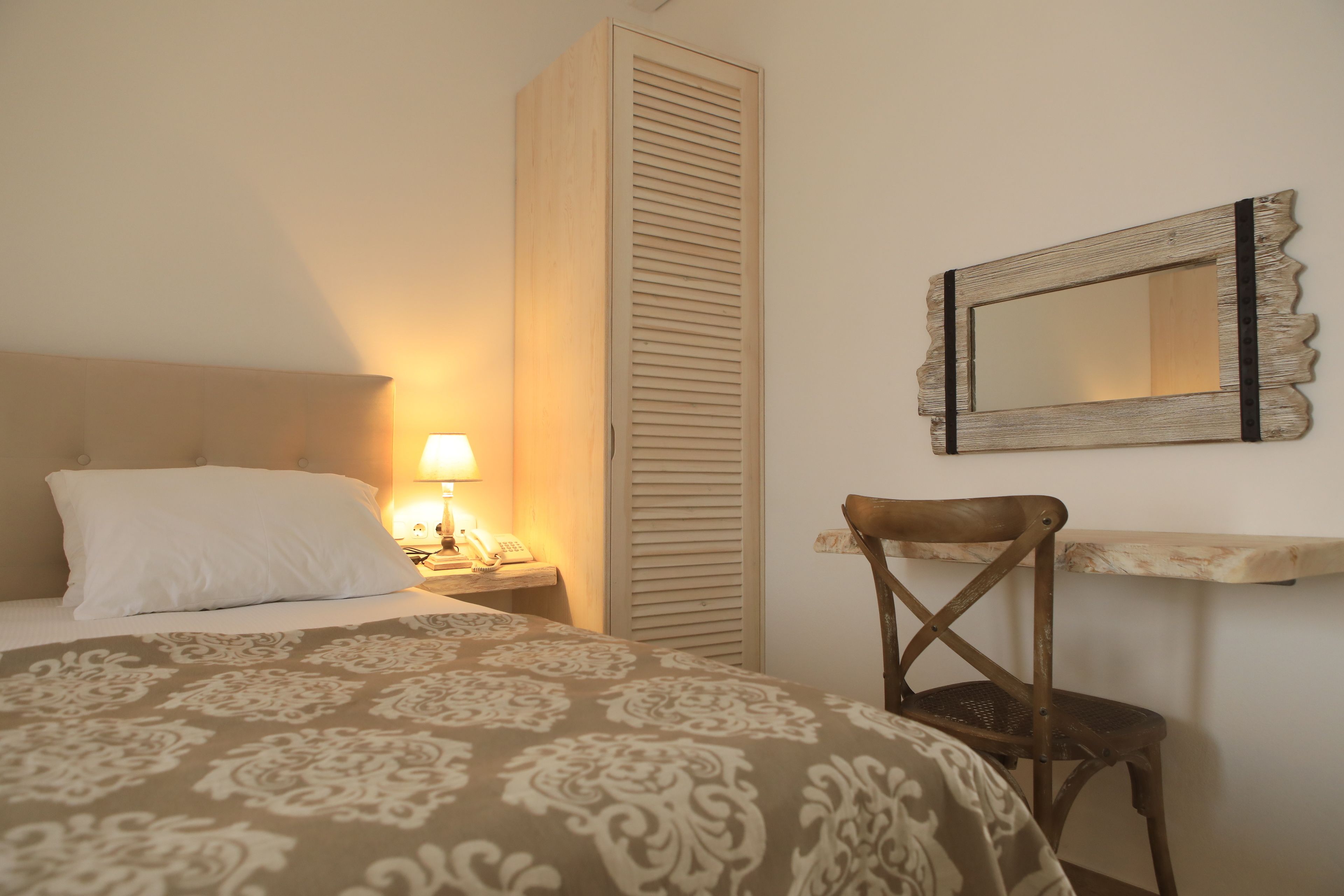 Ein Schlafzimmer mit einem Bett, einer Nachttischlampe, einem Holzsessel, einem Kleiderschrank und einem Spiegel an der Wand.