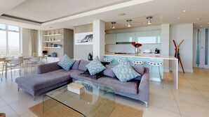 A modern living room with a sectional sofa, a glass coffee table, and a dining area with a white table and chairs. - Horizon Bay 1602 (Cape Town)
