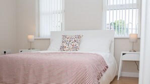 A bedroom with a bed, two bedside tables, a window with blinds, and a lamp on each table.