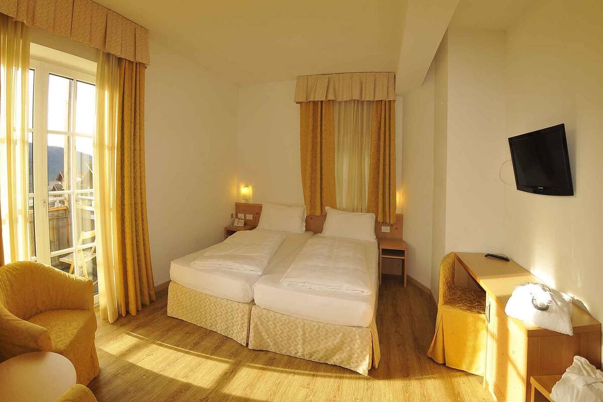 Habitación de hotel con dos camas, un escritorio, una silla, televisión y vistas al balcón.