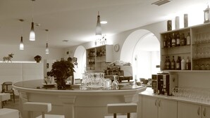 A bar area with a round table, multiple chairs, and a variety of bottles and glasses on shelves. - Alpen Hotel Eghel (Folgaria)