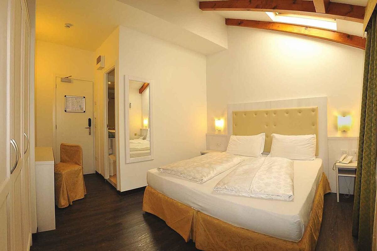 Una habitación de hotel con una cama doble, un pequeño escritorio con teléfono, una silla y un espejo.