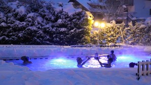 A snow-covered outdoor area with a pool, surrounded by snow-laden trees and a building in the background. - Alpen Hotel Eghel (Folgaria)