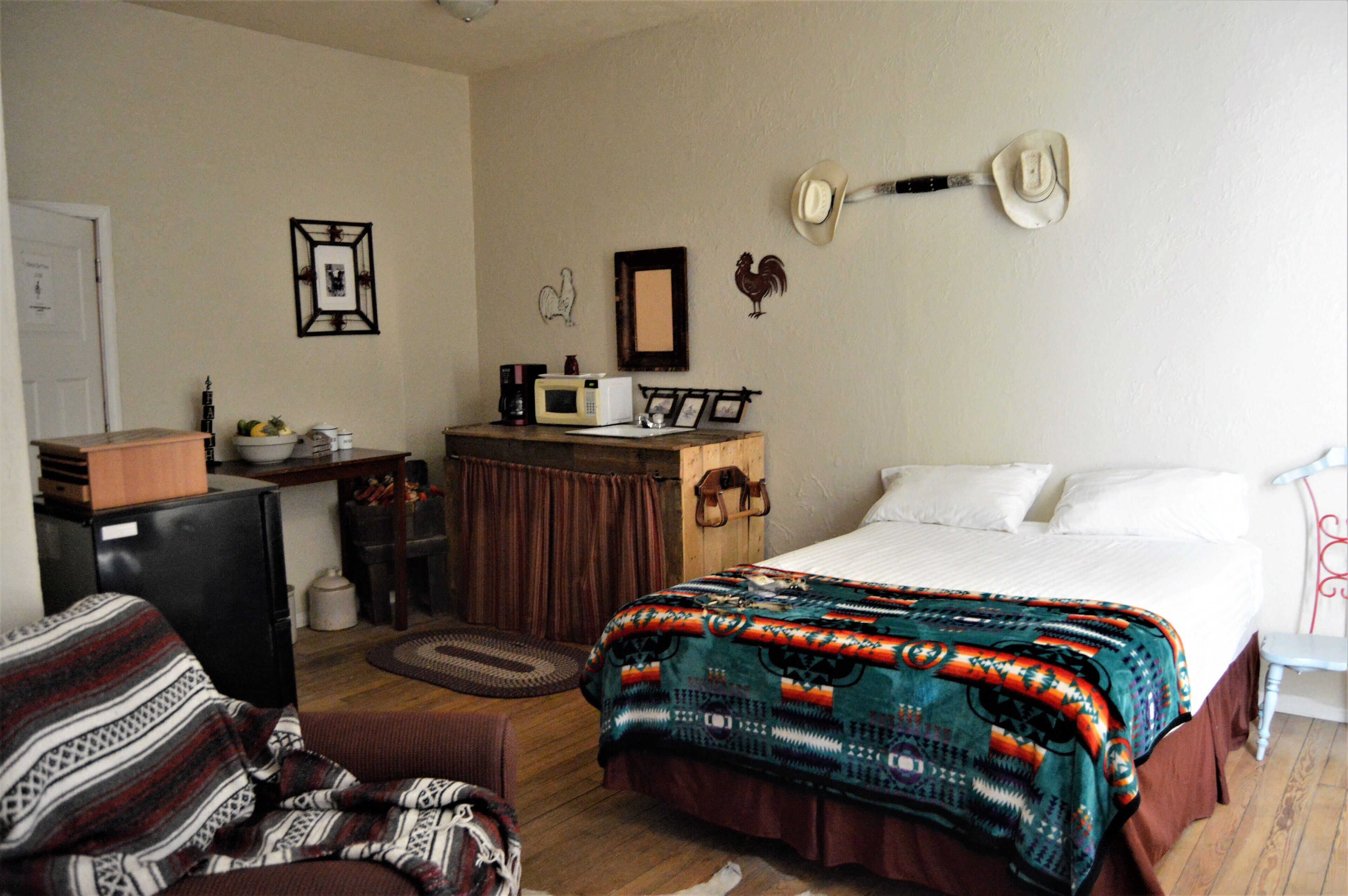 Een kamer met een bed, een bureau, een stoel en een klein kitchenette.