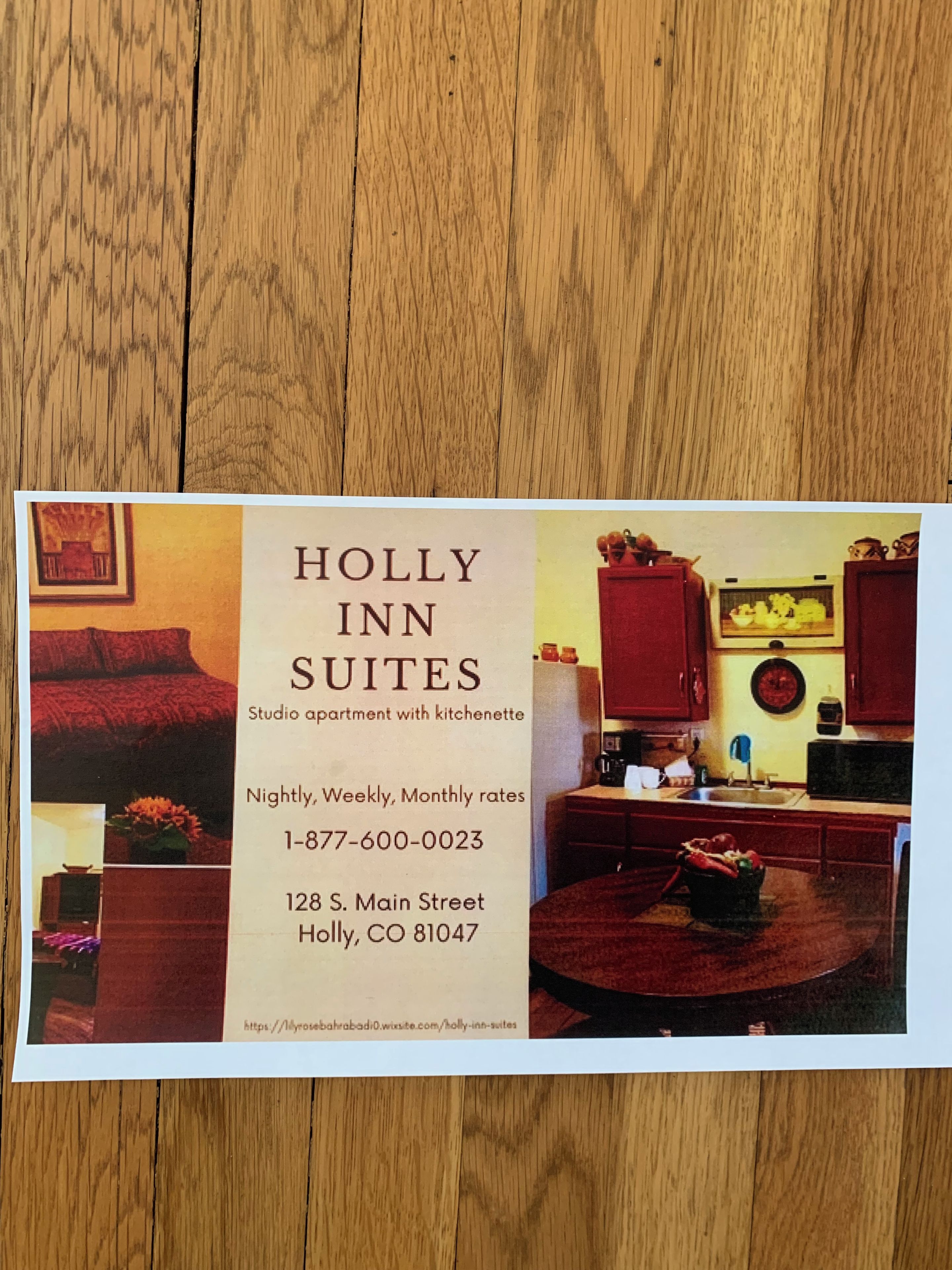 Werbung für Holly Inn Suites: Ein Studioapartment mit Küchenzeile, inklusive eines Essbereichs mit rotem Tisch und Stühlen, einer Küche mit Schränken und einer Mikrowelle sowie einer Wohnbereiches mit rotem Sofa und Kamin.