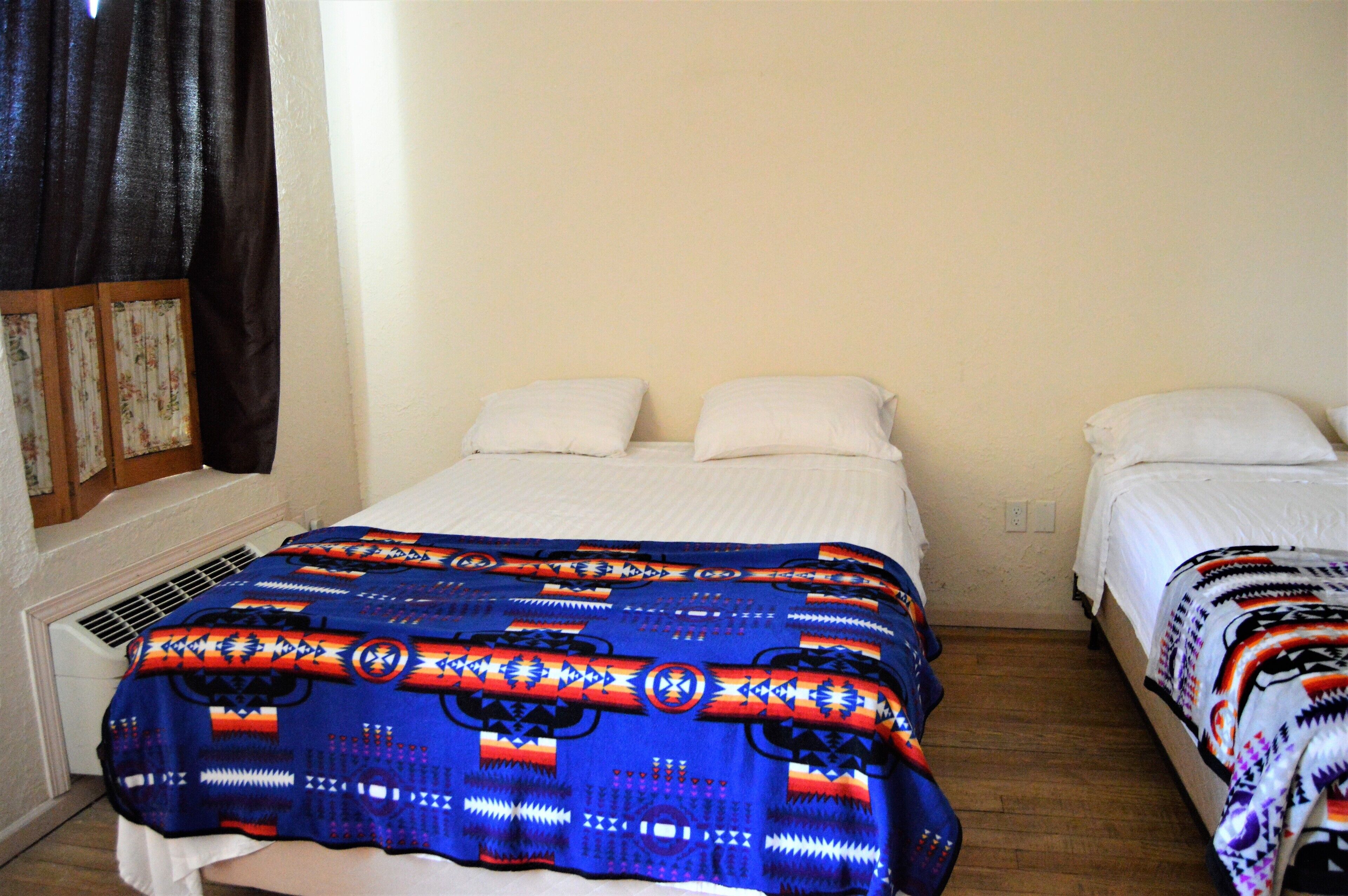 A room with two beds, one with a blue patterned blanket and the other with a white blanket.