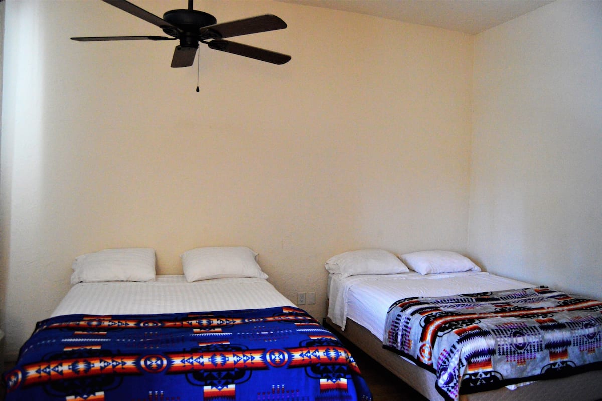 A bedroom with two beds, a ceiling fan, and plain walls.