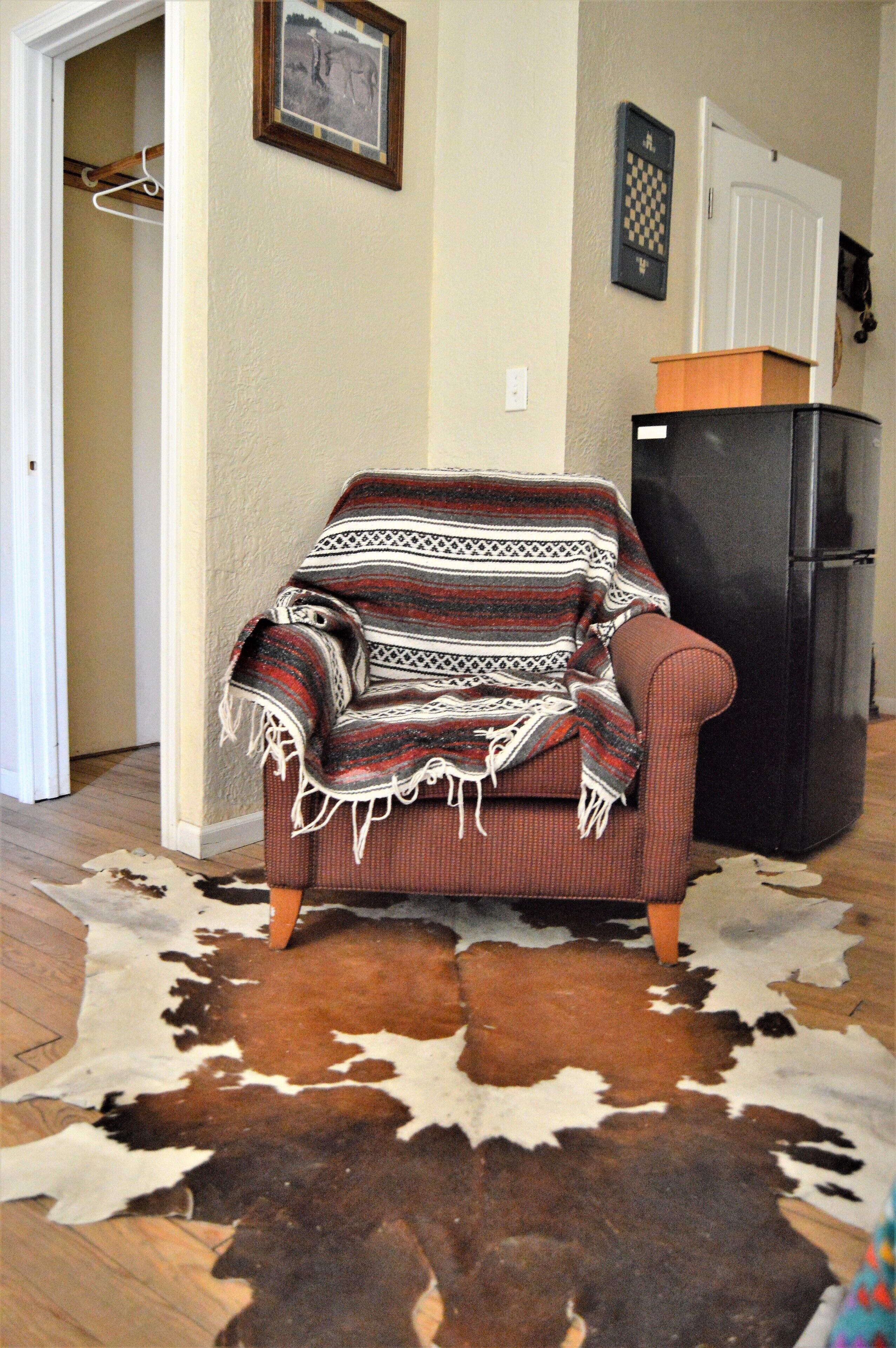A room with a patterned sofa, a black refrigerator, and a cowhide rug.