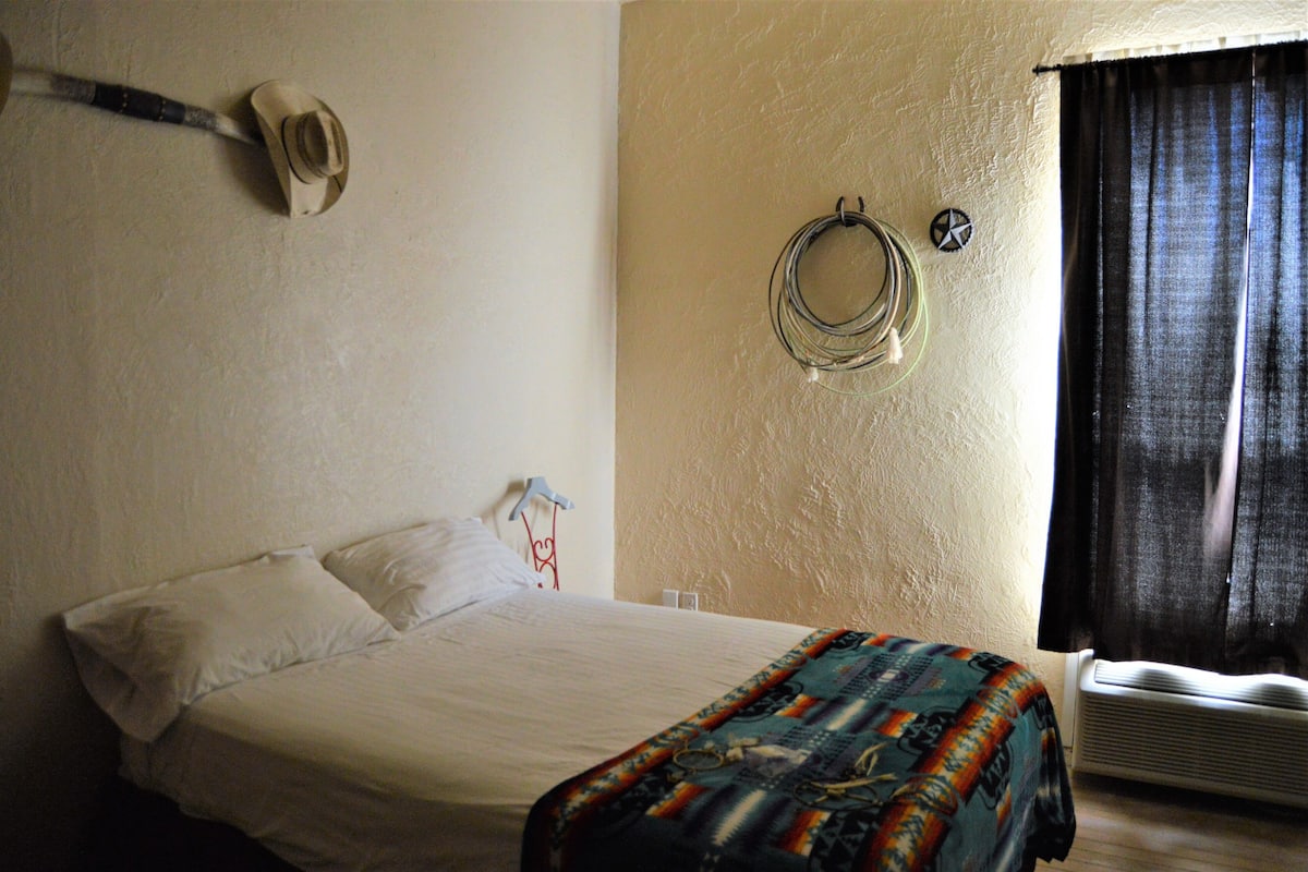 A bedroom with a bed, a wall-mounted hat, a coiled cable, and a window with curtains.