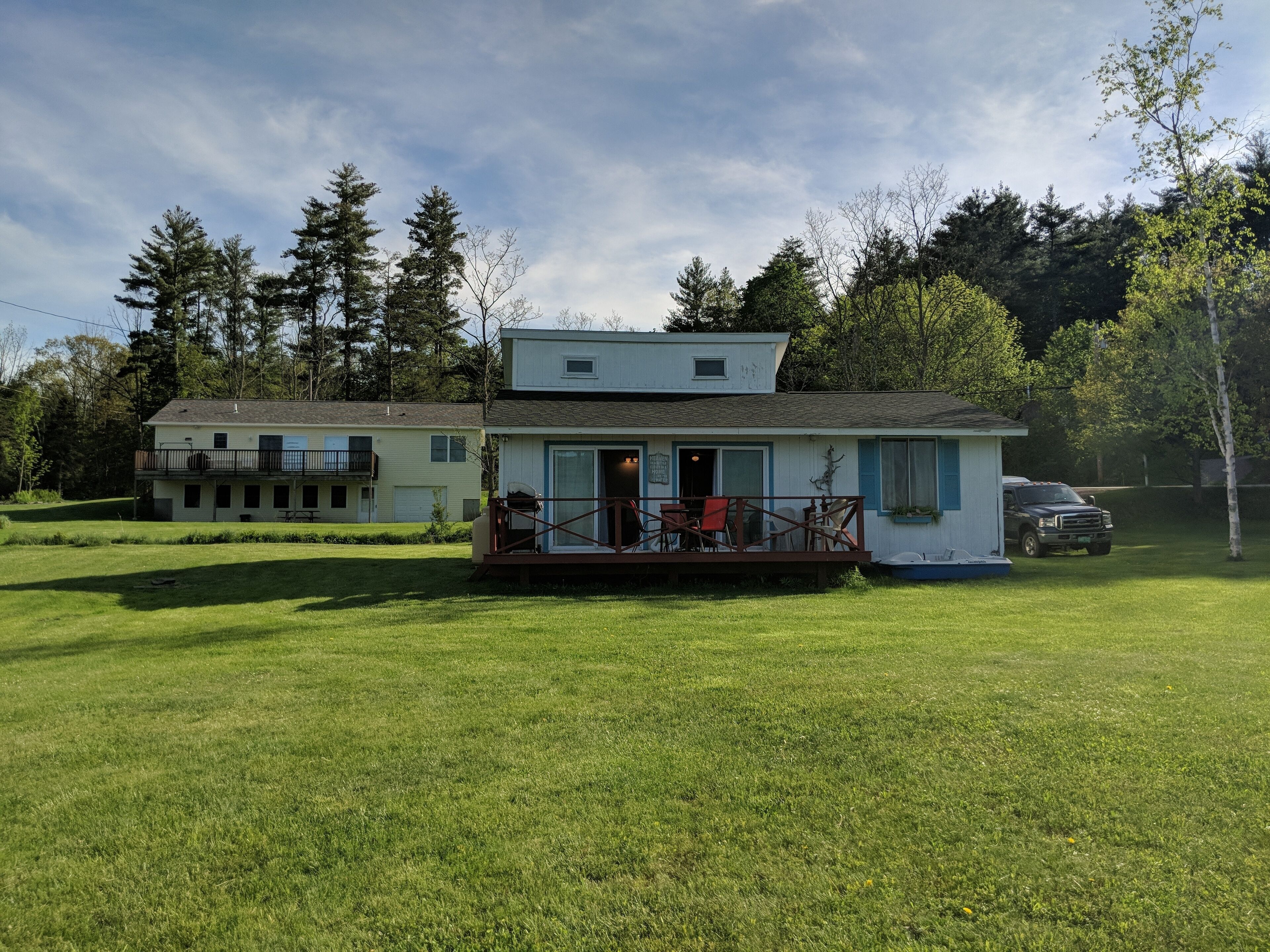 A two-story house with a porch, a deck, and a vehicle parked nearby.