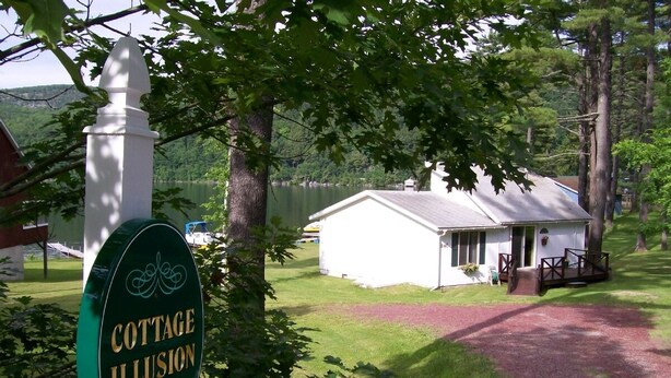 A cottage with a white exterior, a porch, and a sign that reads "COTTAGE ILLUSION 94c". - Lakefront Cottage w/Breathtaking Views! Hiking.PaddleBoat.Doc.Fishing.WiFi (Wells)