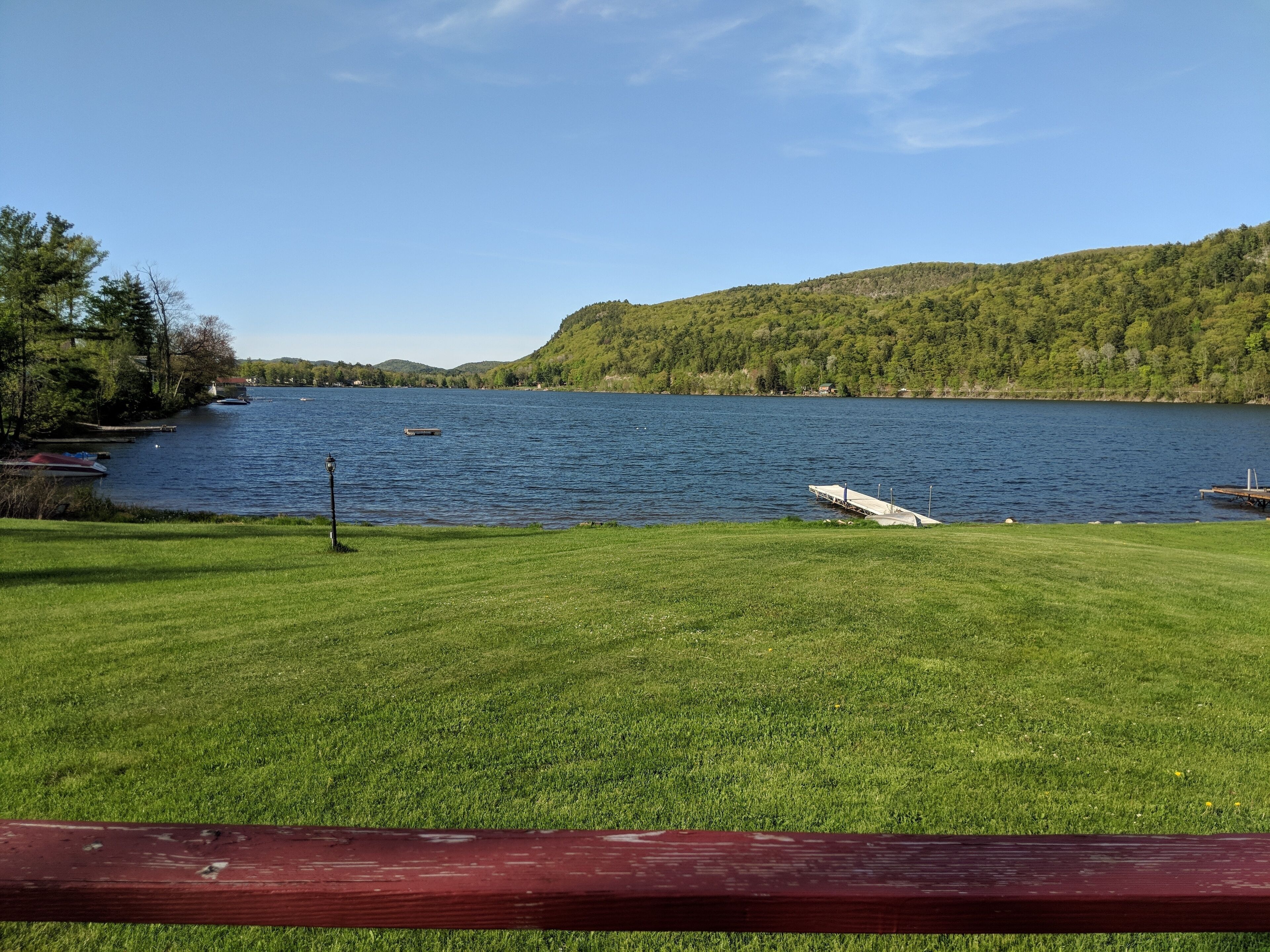 Une zone herbeuse avec une jetée qui s’avance dans un lac, le tout entouré de collines et d’arbres.