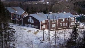 A cluster of wooden houses with large windows and a garage, surrounded by snow-covered ground and trees, with a mountainous backdrop. - Lakefront Cottage w/Breathtaking Views! Hiking.PaddleBoat.Doc.Fishing.WiFi (Wells)