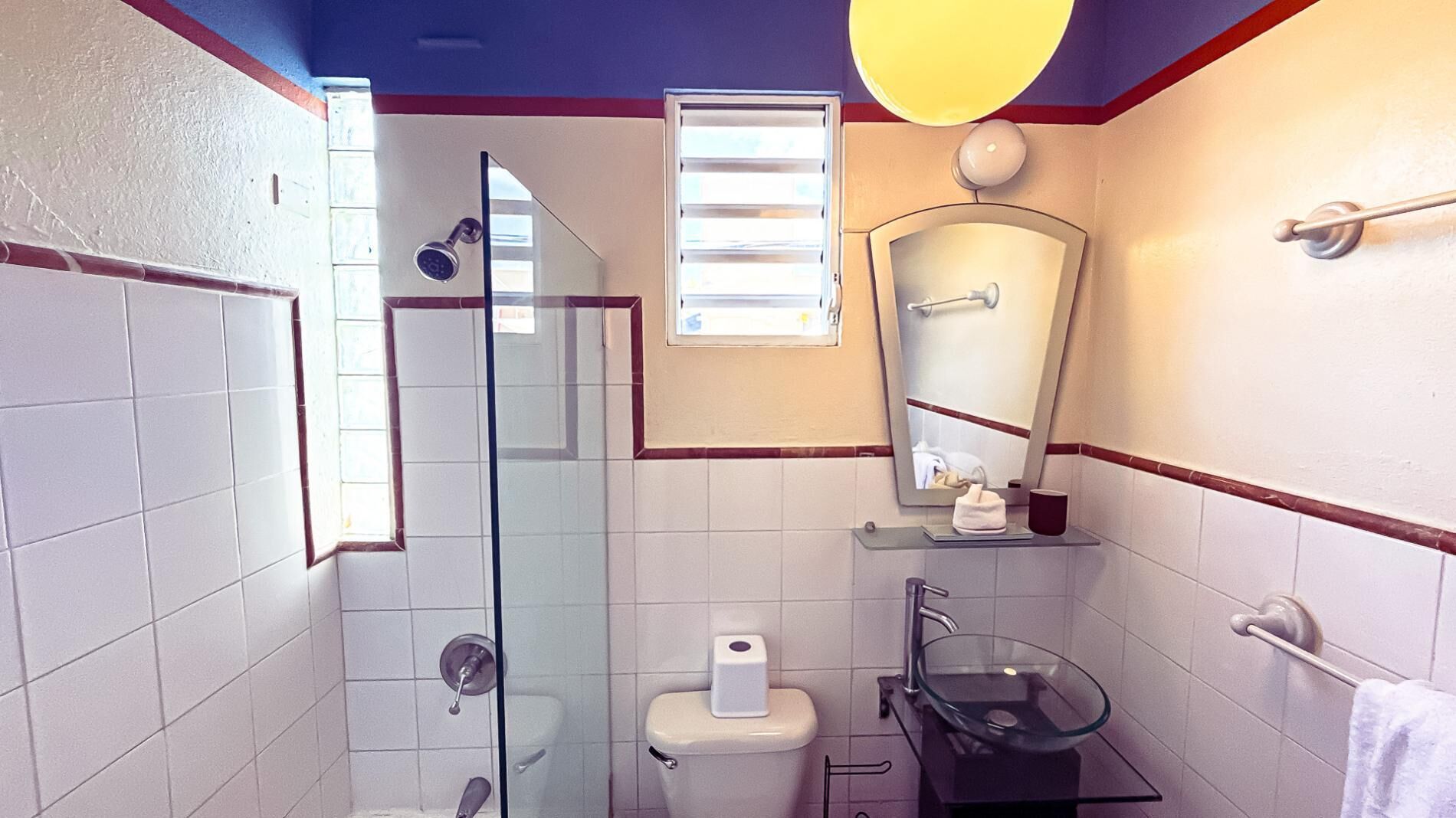 Een badkamer met een glazen douchecabine, toilet, wastafel met een glazen wasbak en een spiegel boven de wastafel.