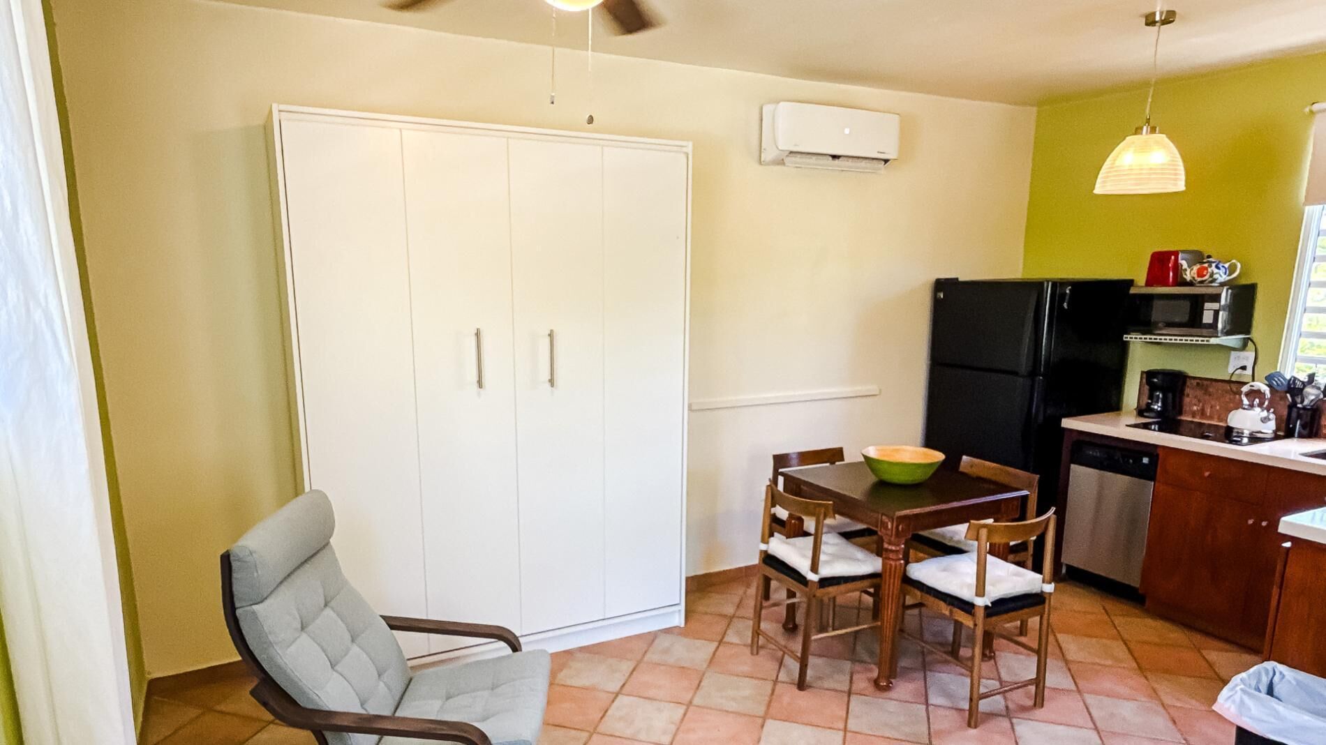 Une cuisine compacte comprenant une table à manger, des chaises, un réfrigérateur et un ventilateur de plafond.