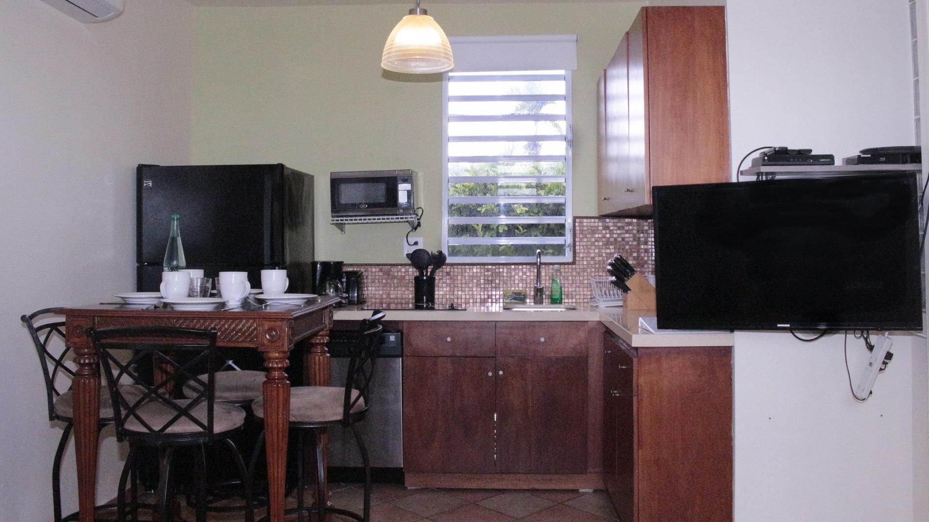 A compact kitchen with a dining area, a microwave, a sink, and a television mounted on the wall.
