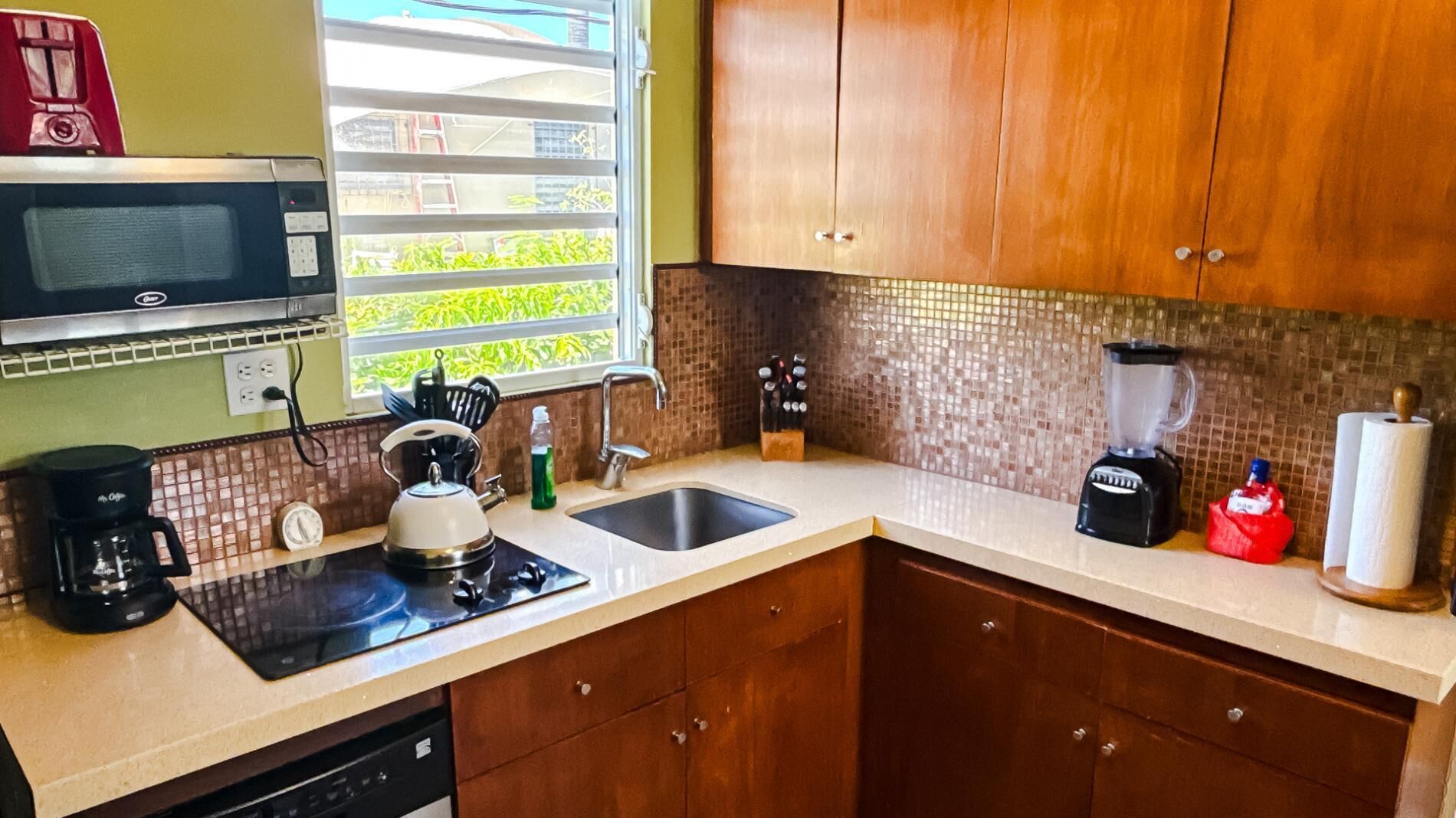 A kitchen with a microwave, kettle, sink, blender, and coffee maker.