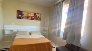 A bedroom with a bed, a ceiling fan, a window with curtains, and a wall-mounted artwork. - Family apartments - air conditioning, fan, internet... fully furnished. (Arraial do Cabo)